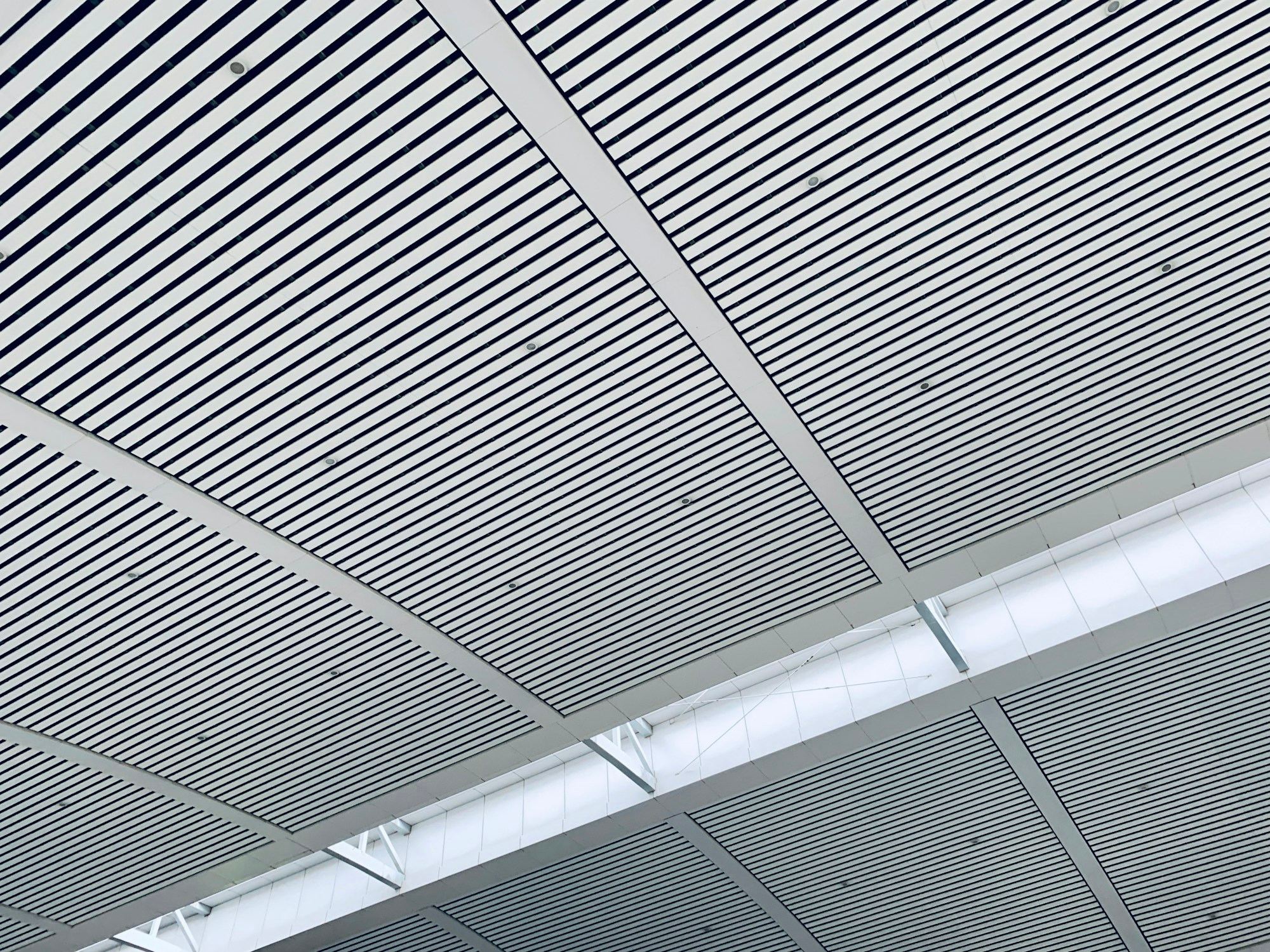 A white linear strip ceiling, its slats running toward a line of light.