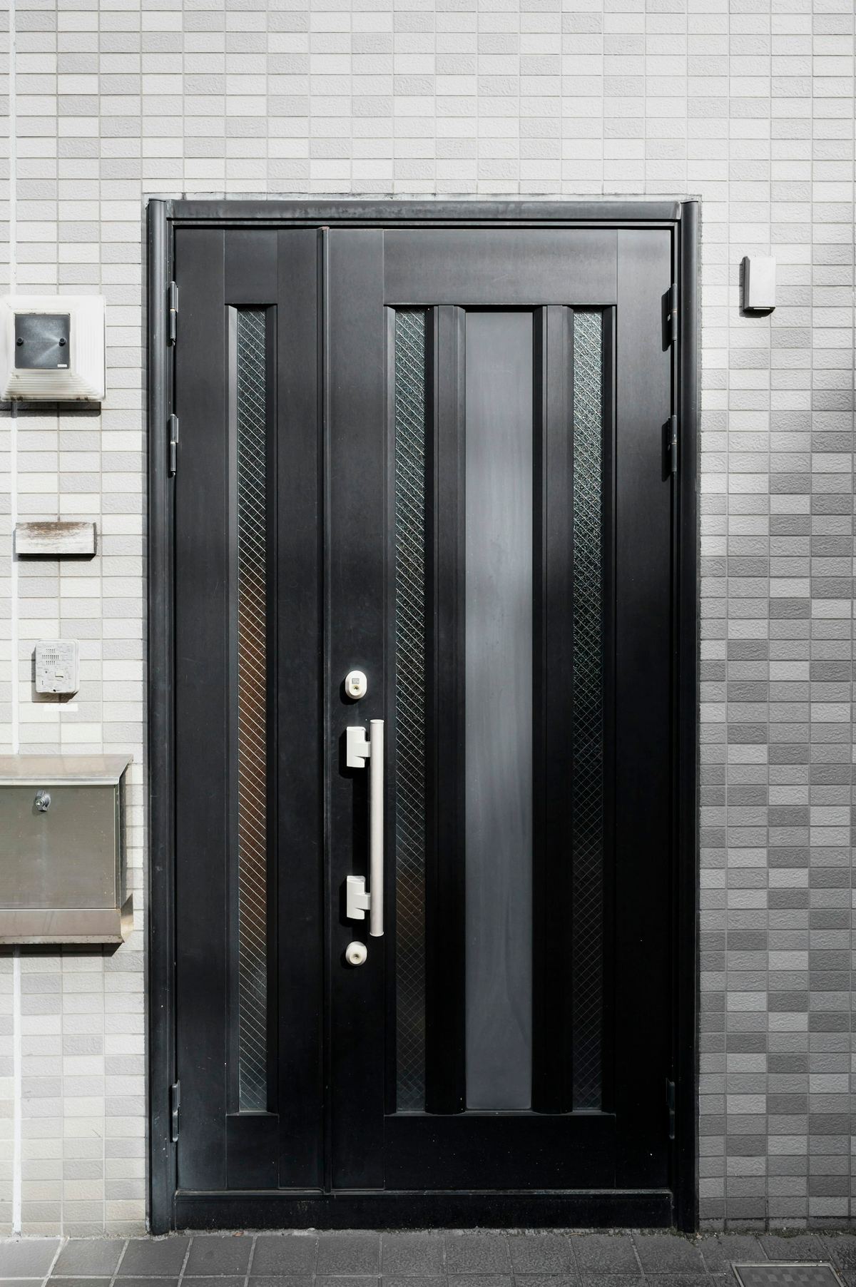 A black entrance door with narrow vertical glass panels and a steel handle.