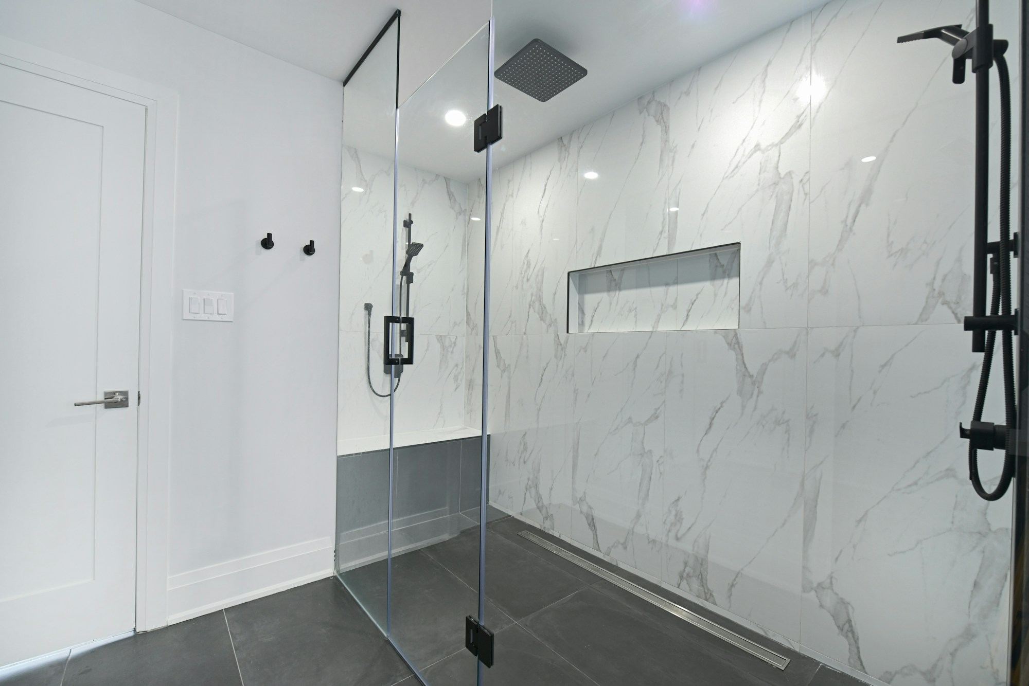 A walk-in shower behind a frameless glass screen, with marble walls.