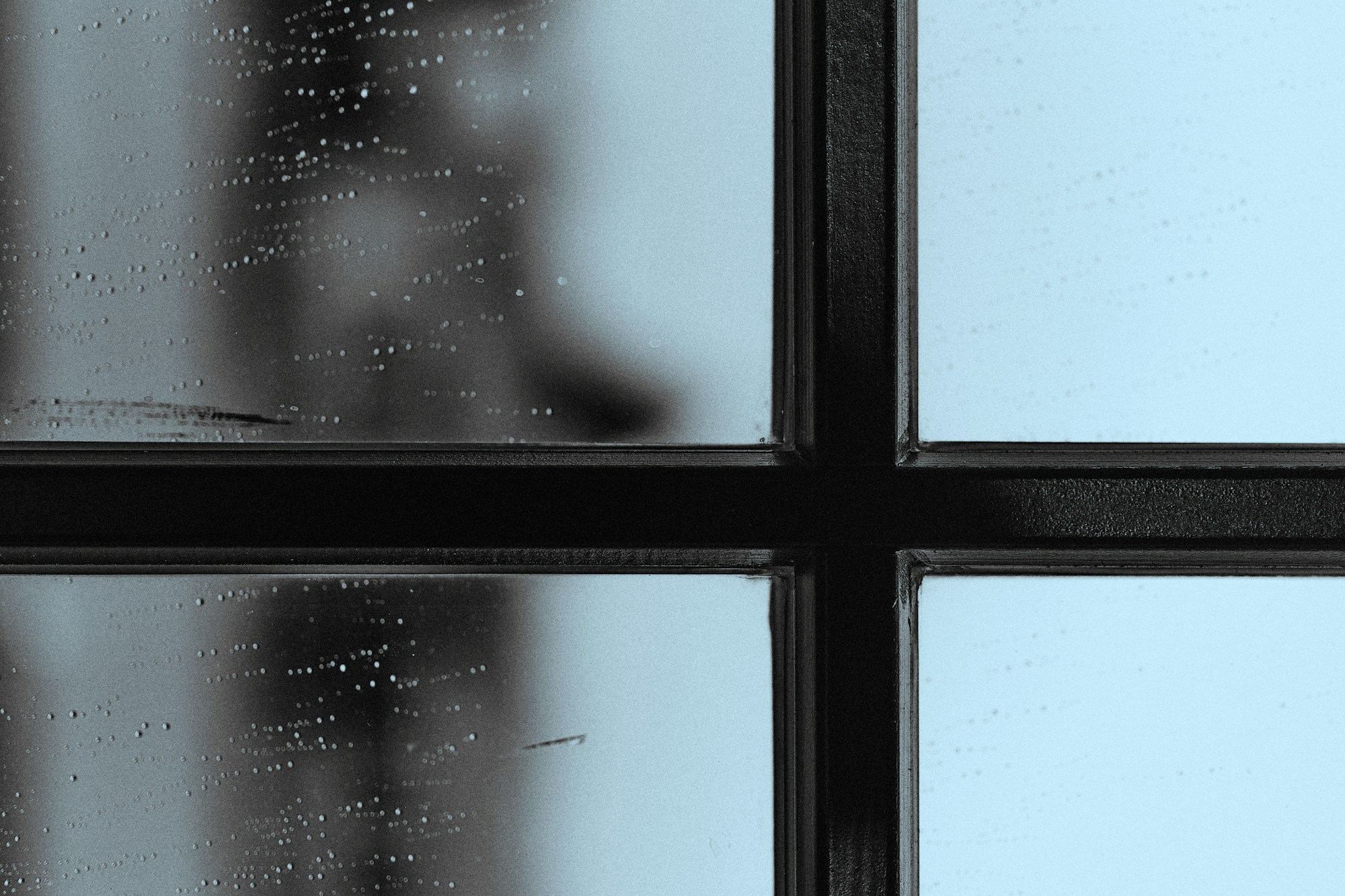 Rain on a window pane, seen close up against its black metal frame.